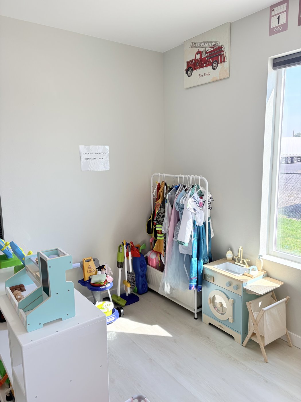 Dramatic play corner with a dress-up rack, play washer, toy market stand and cleaning toys